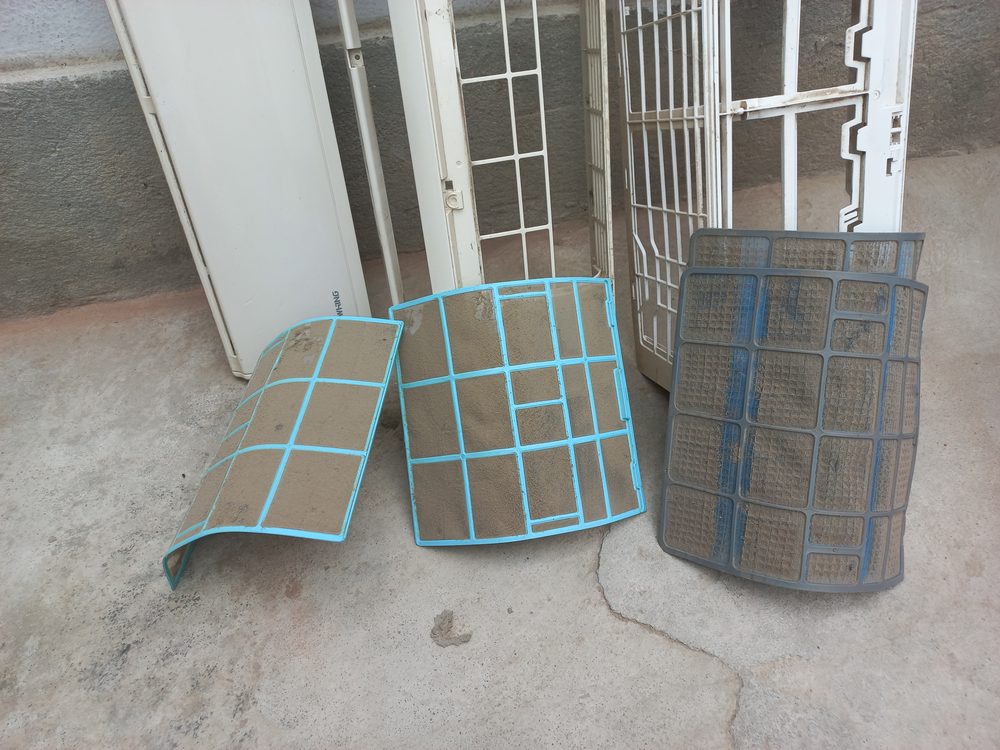 Três filtros de ar condicionado sujos ao lado das peças de uma unidade interior desmontada
